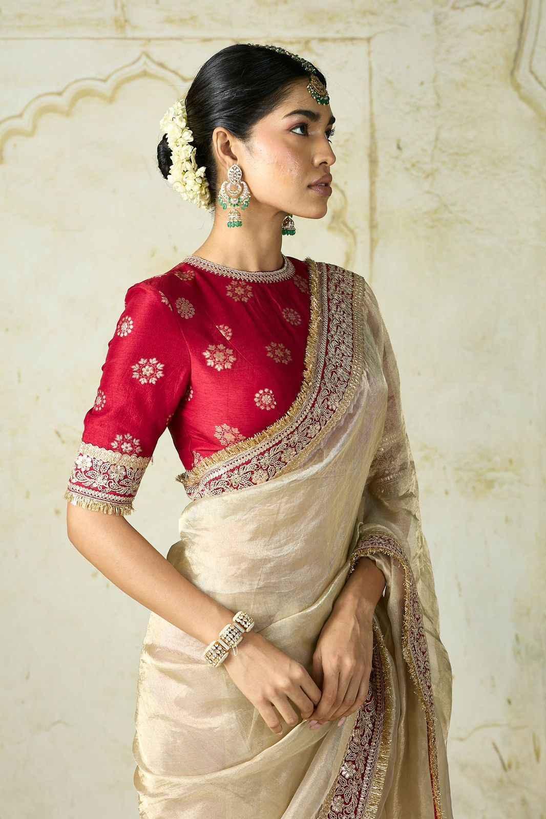 Woman in beige silk saree with gold embroidery and red blouse, traditional Indian jewelry and floral hair adornment