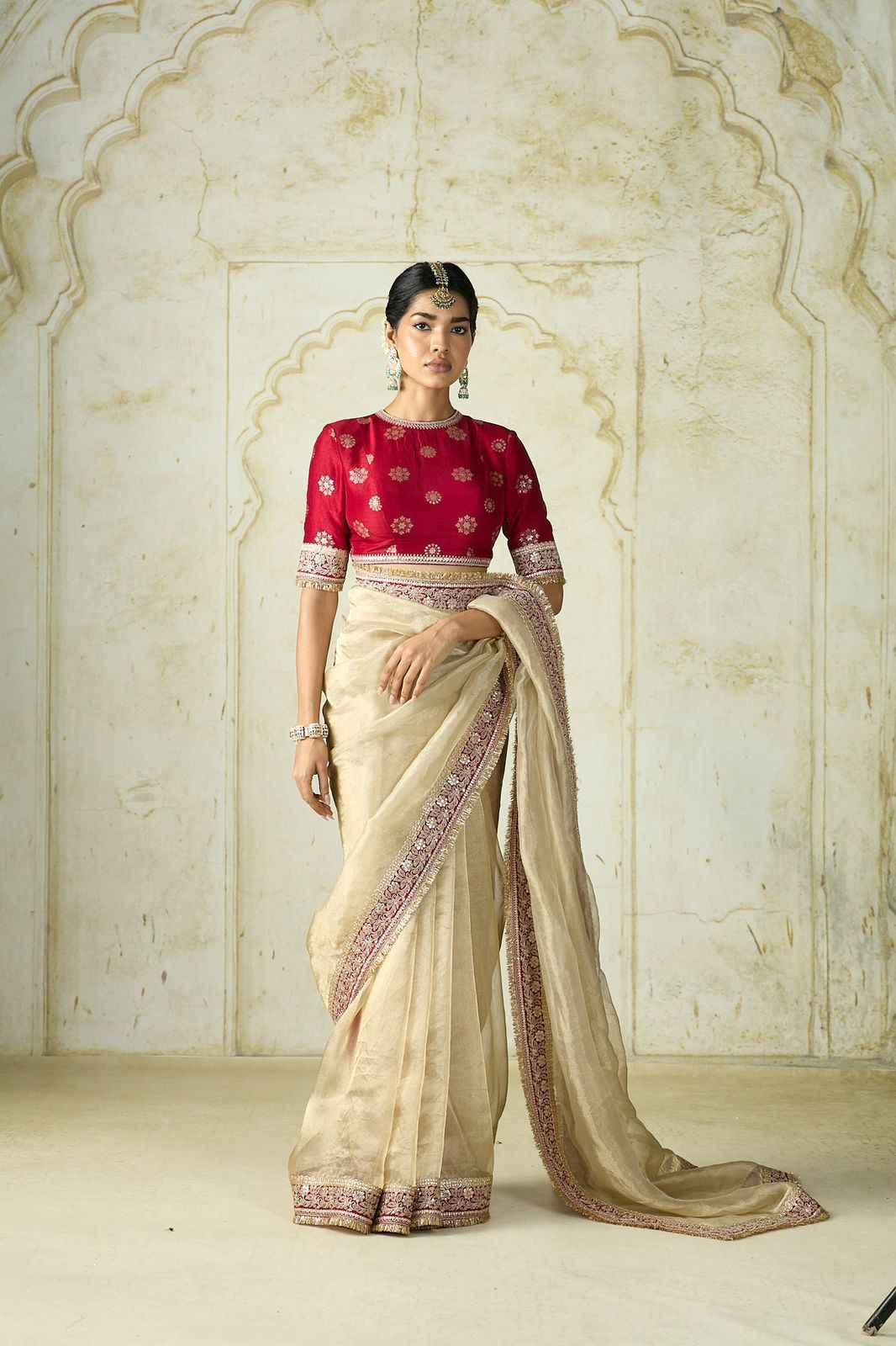 Elegant woman wearing a beige silk saree with sequin embroidery and a red embroidered blouse in a traditional setting
