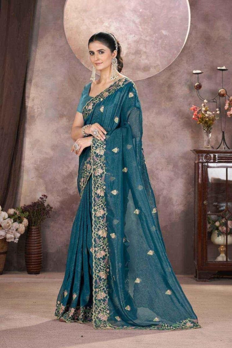 Teal embroidered saree with gold border and short-sleeve blouse, standing drape.