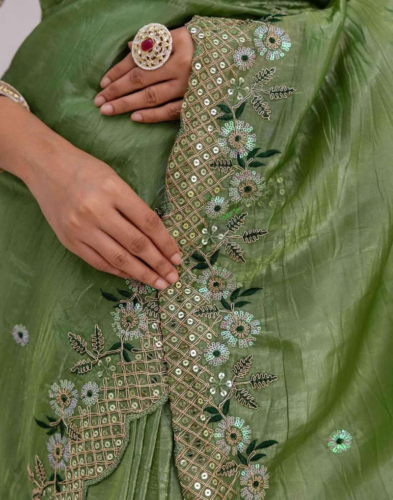 Green fabric close-up with gold-toned floral and grid embroidery, embellished center