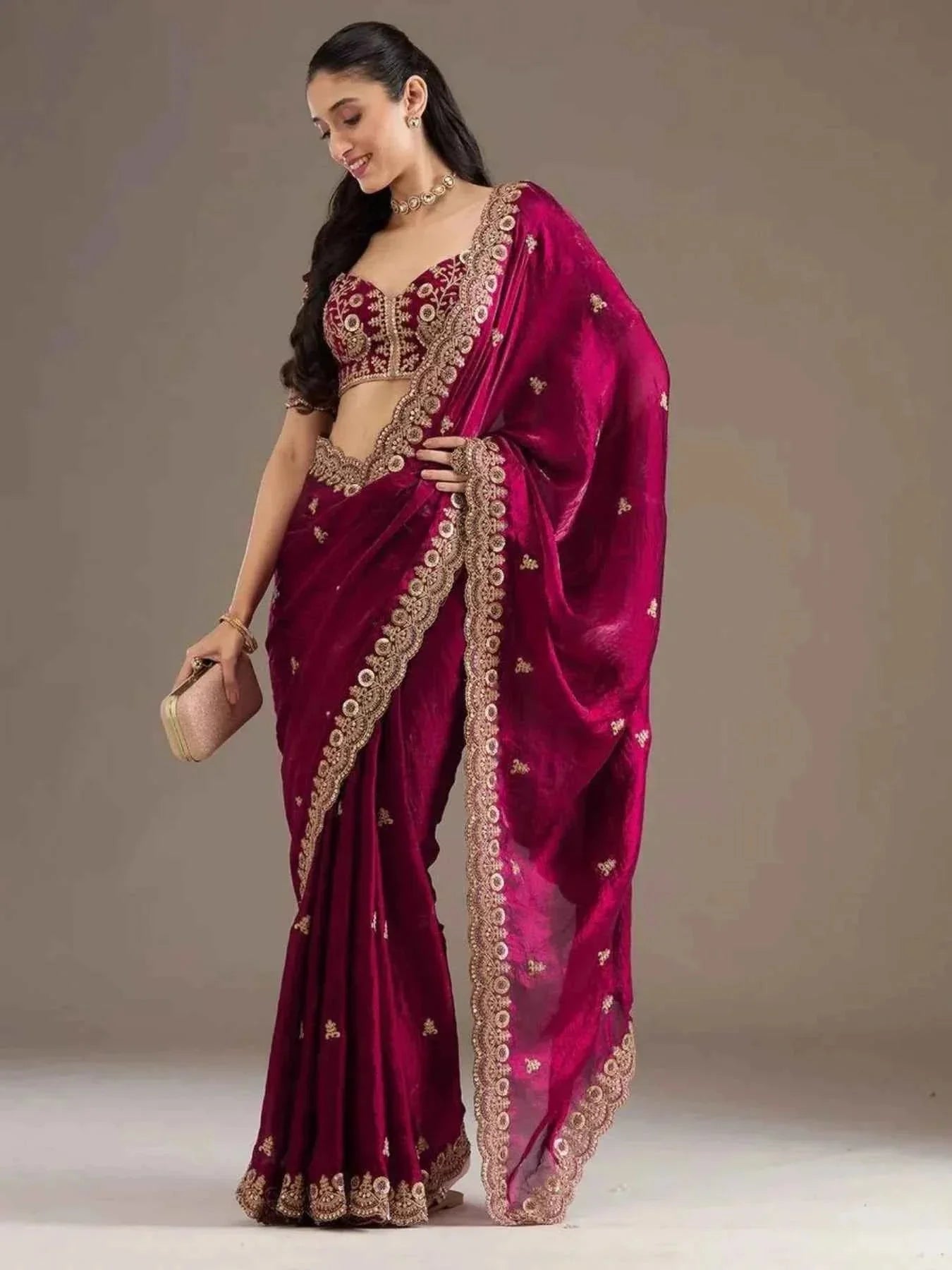 Woman wearing hot pink satin silk saree with heavy jari cutwork embroidery, holding clutch