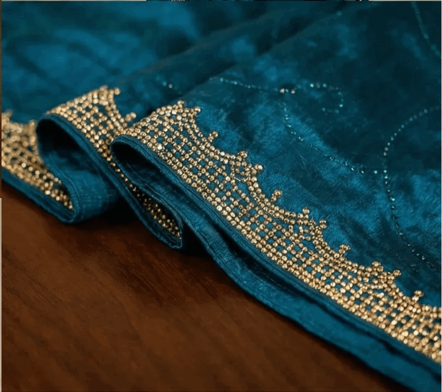 Deep teal blue saree fabric with shimmering texture and detailed gold-toned stone trim