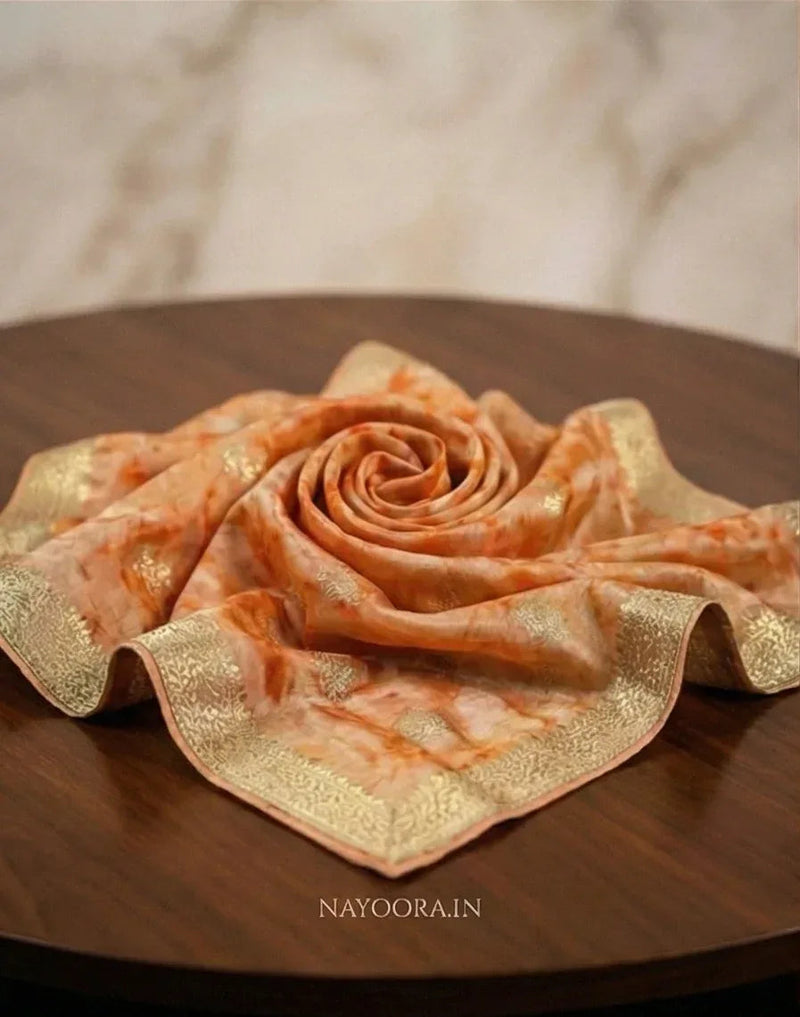 Peach shibori printed silk saree folded into a rose shape with gold border