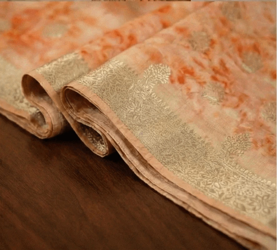 Peach shibori printed saree fabric with ornate gold zari border detail