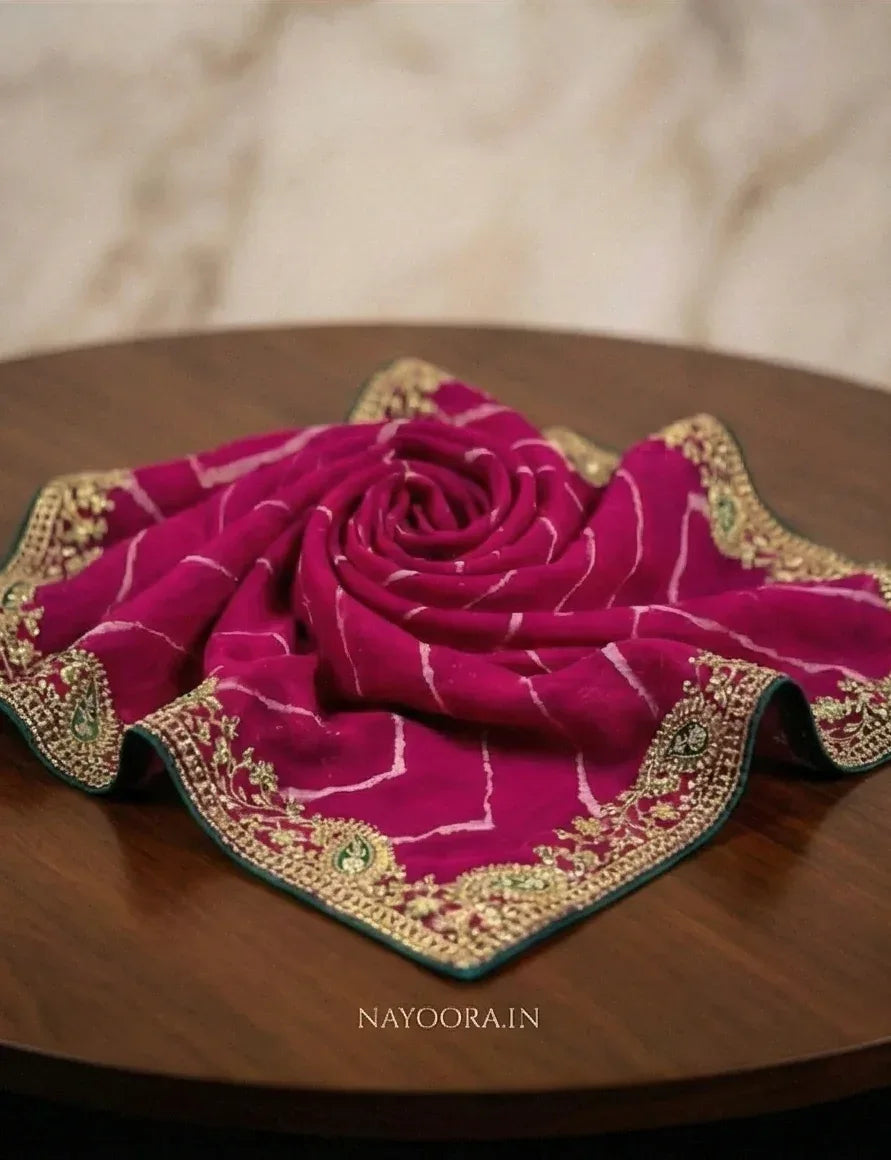 Rani pink georgette saree with decorative green-edged border, folded on table