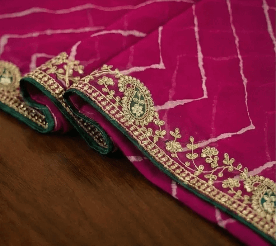 Rani pink georgette saree border close-up with gold embroidery and green trim