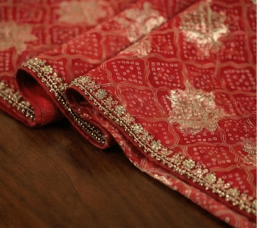 Red saree hem close-up with gold beaded trim and bandhani motif panels