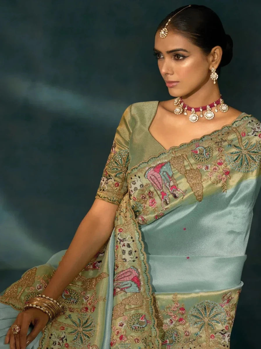 Aqua blue saree draped over shoulder with gold border and pink-green embroidery