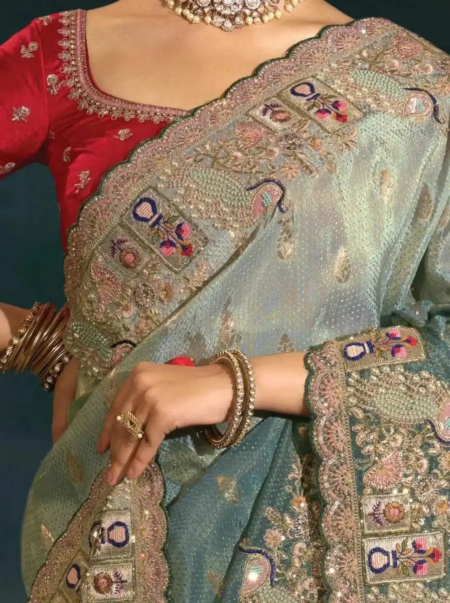 Sage green silk saree with detailed embroidered border and blue-and-red motif panels