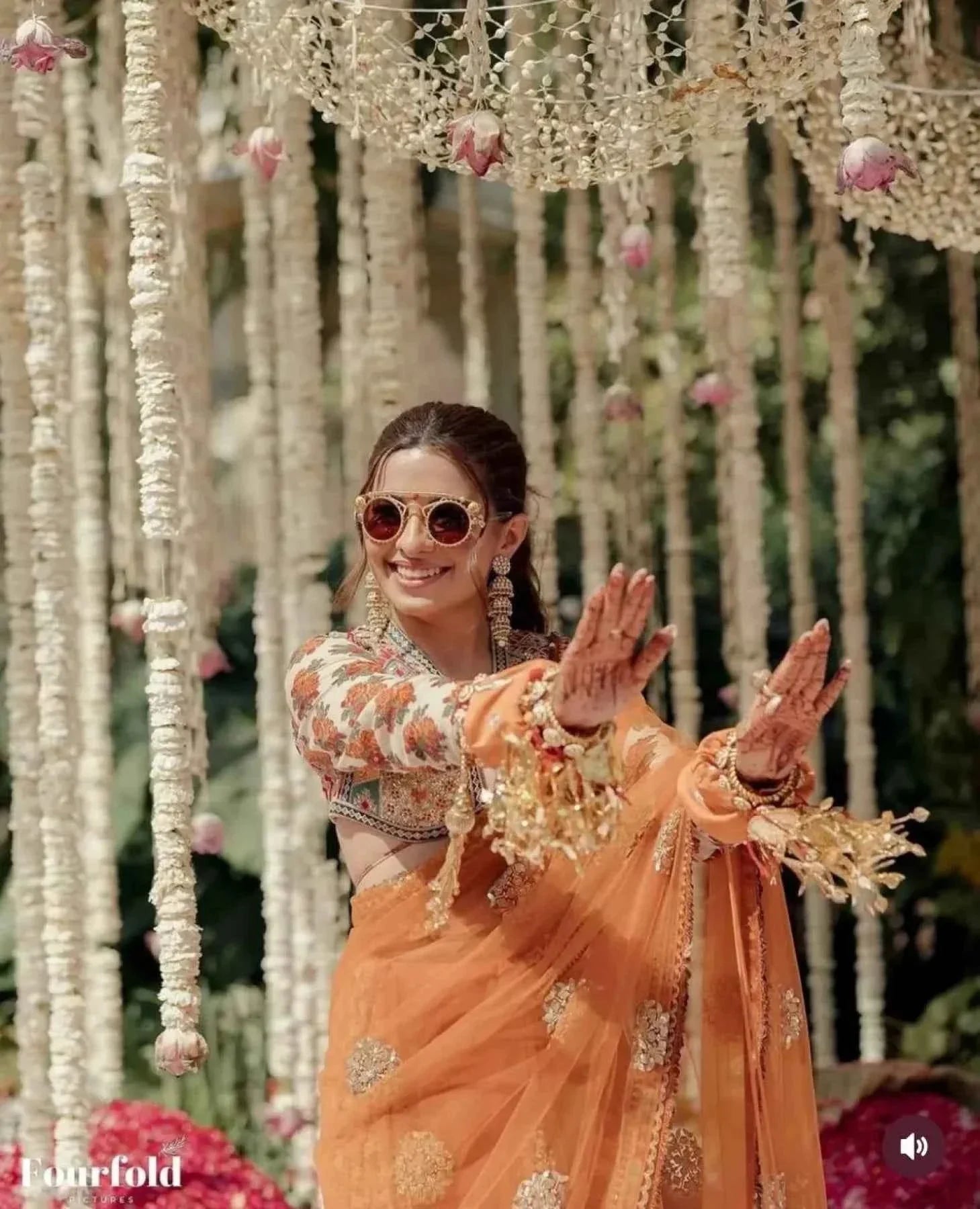 Smiling woman in orange net saree with floral stitched blouse and sunglasses at decorated outdoor event