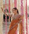 Woman in orange net saree with stitched designer blouse posing among pink and white flower garlands