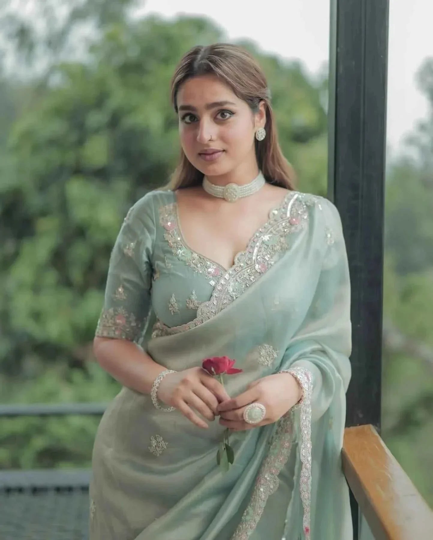 Woman wearing pastel green satin silk saree with sequin cutwork embroidery holding red rose