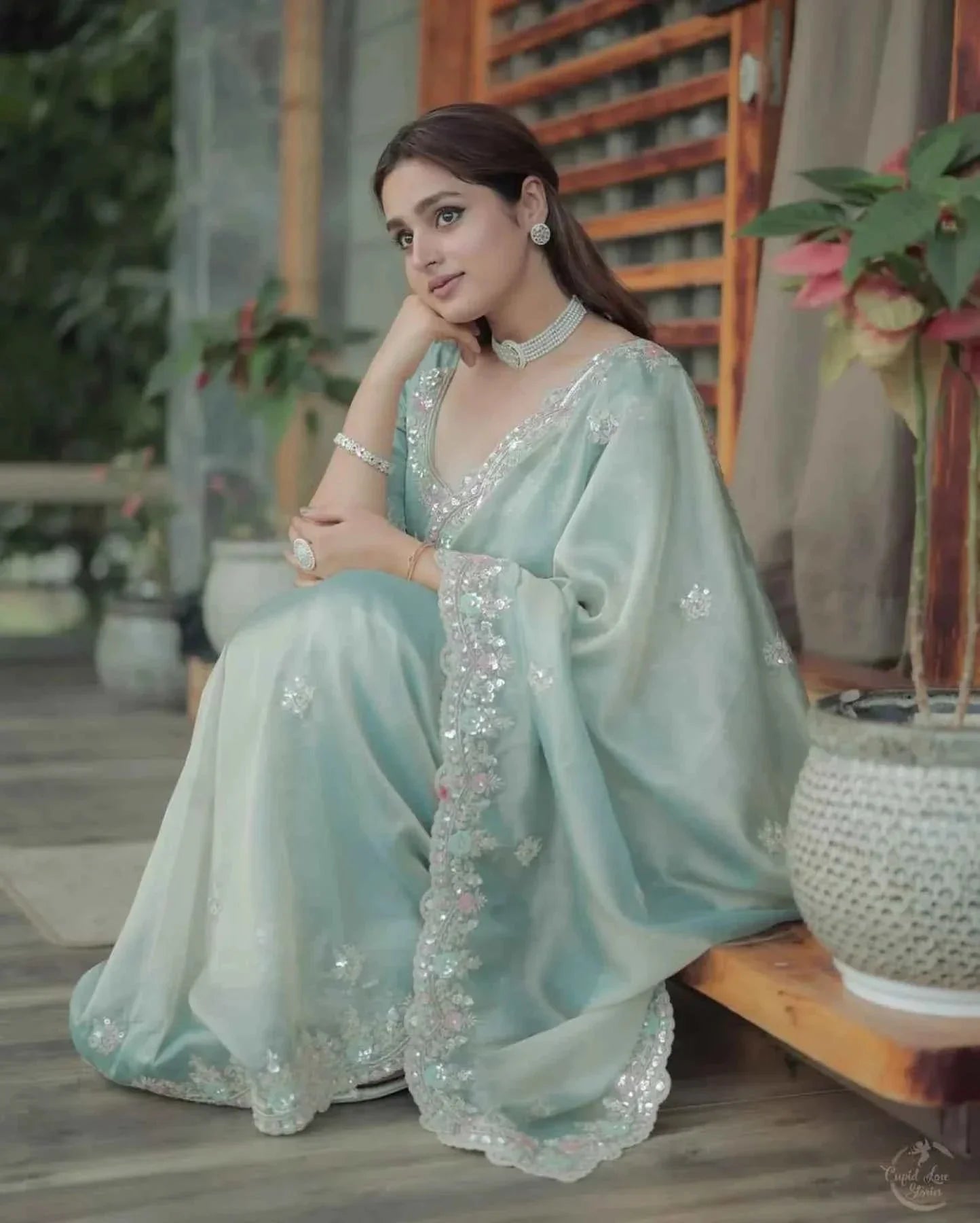 Woman wearing pastel green satin silk saree with sequin cutwork embroidery sitting indoors