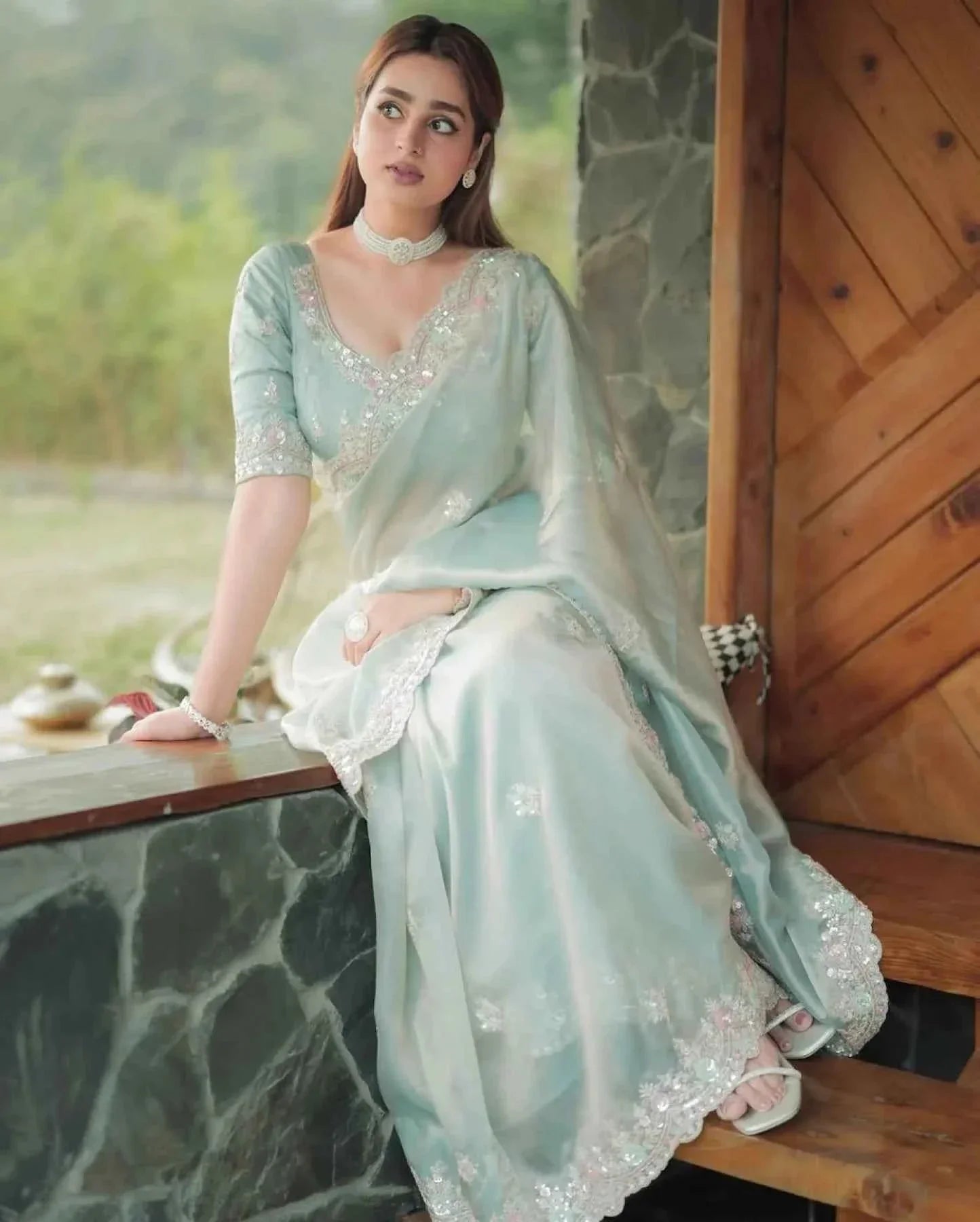 Woman wearing pastel green satin silk saree with sequin cutwork embroidery sitting on stone ledge