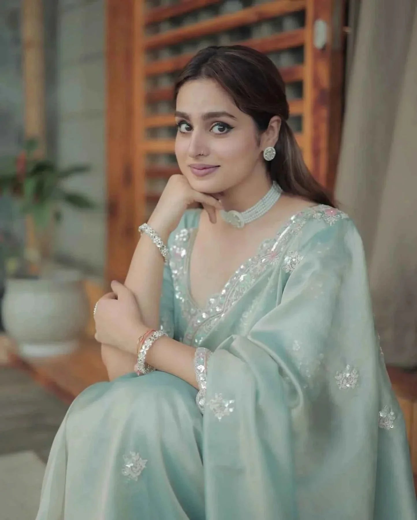 Woman sitting wearing pastel green satin silk saree with sequin cutwork embroidery and silver jewelry