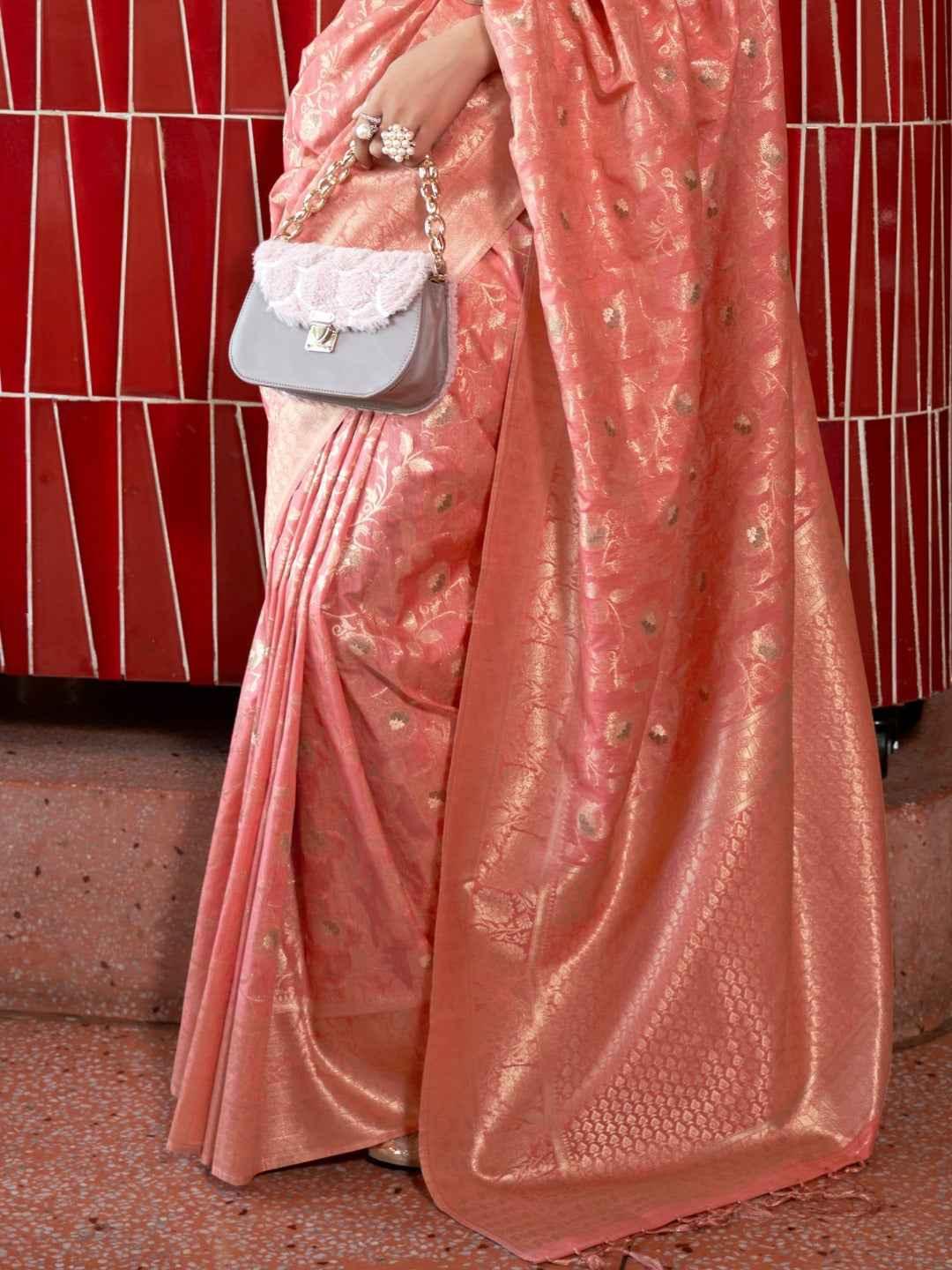 Close-up of a peach Katan silk saree with intricate zari weaving and floral motifs, paired with a gray handbag
