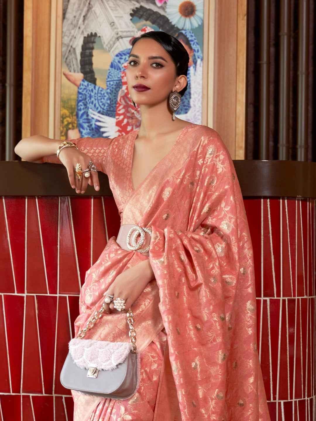 Woman wearing peach Katan silk saree with zari weaving and silver belt, holding grey handbag