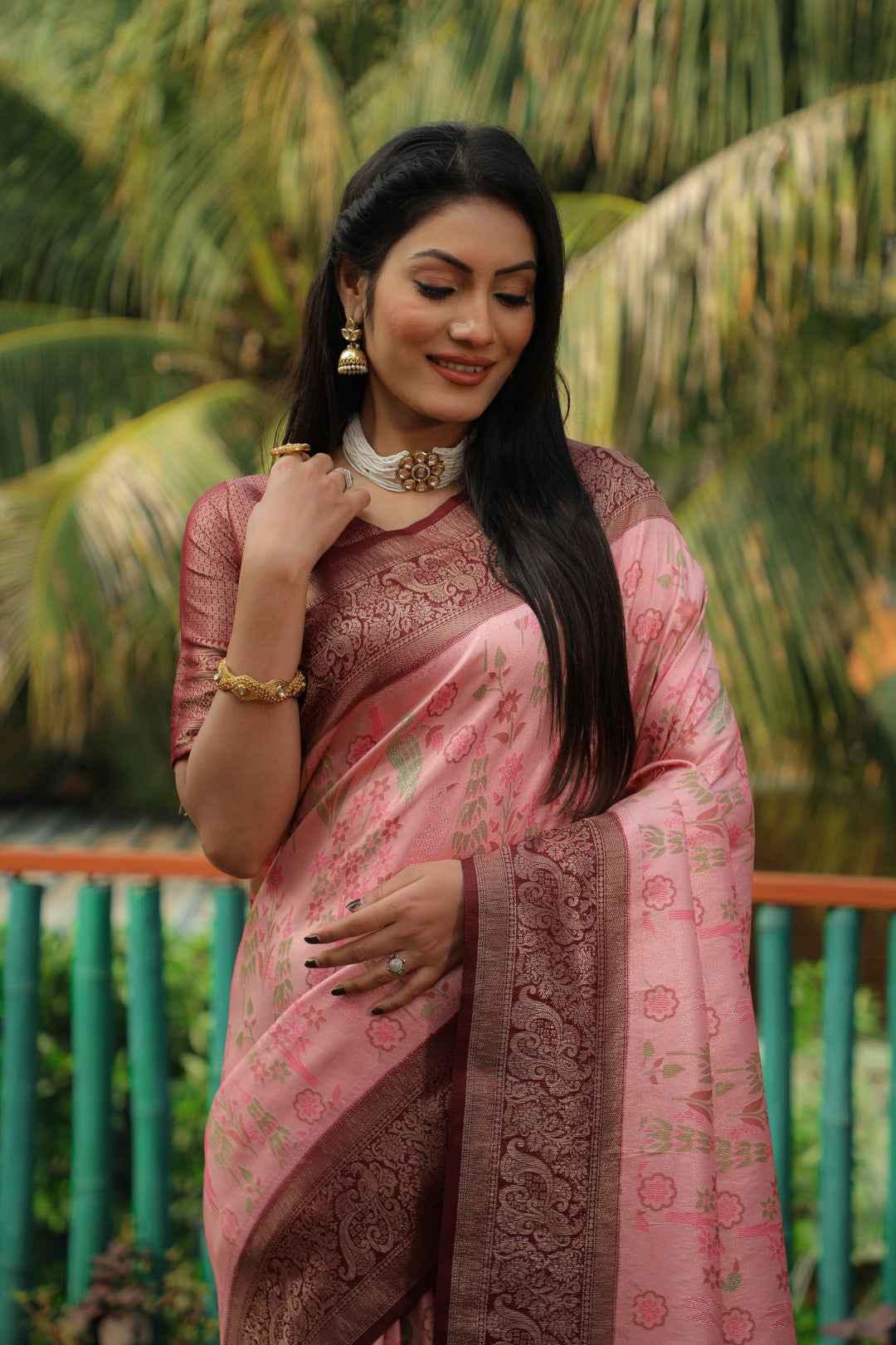 Woman wearing pink Kanjivaram silk saree with zari weaving and floral motifs, standing outdoors
