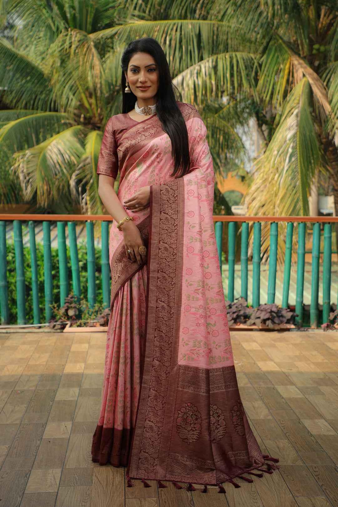 Woman wearing pink and brown Kanjivaram silk saree with intricate zari weaving, standing outdoors against palm trees