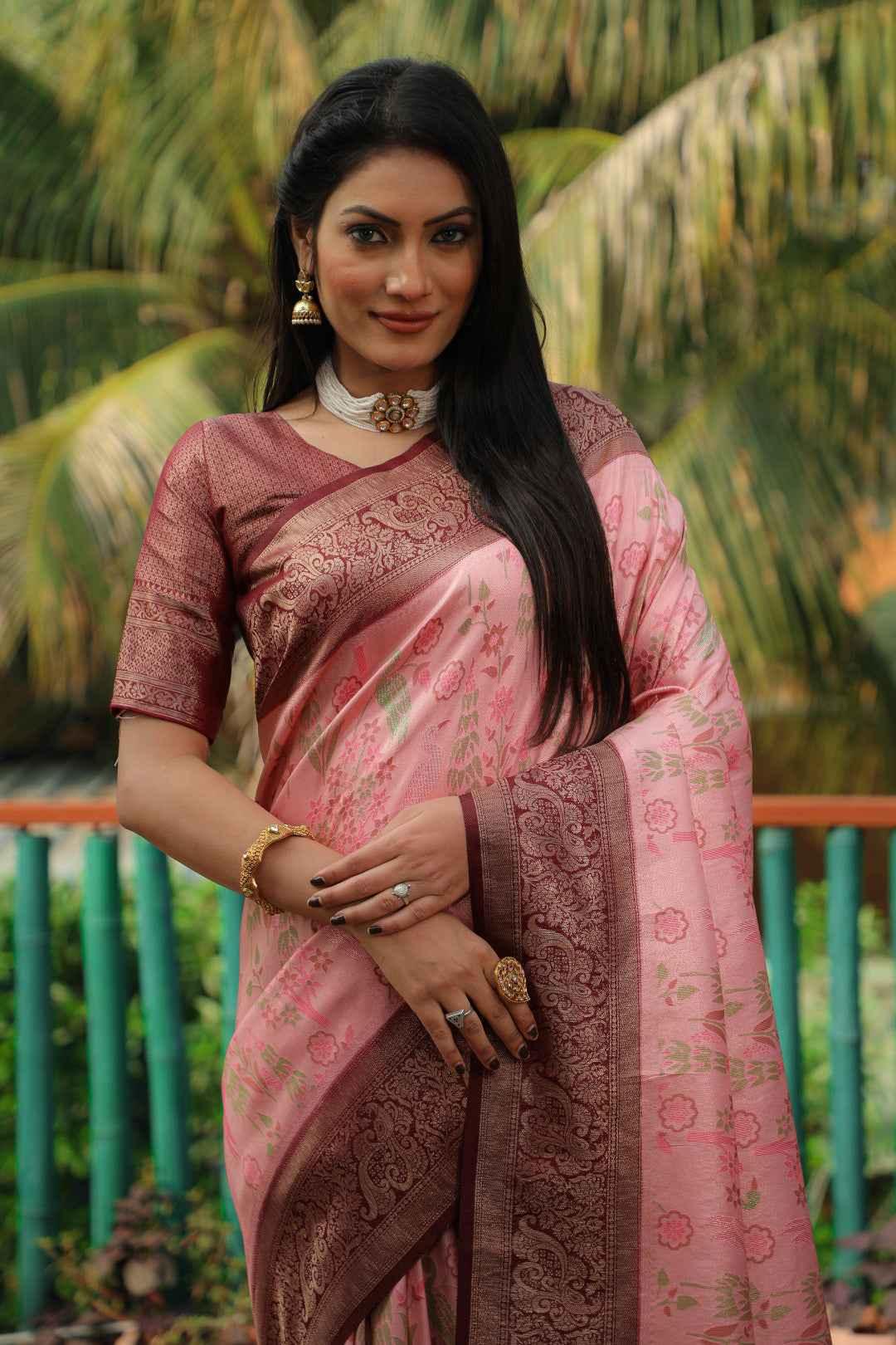 Woman in pink Kanjivaram silk saree with intricate zari floral design and maroon blouse, outdoor setting