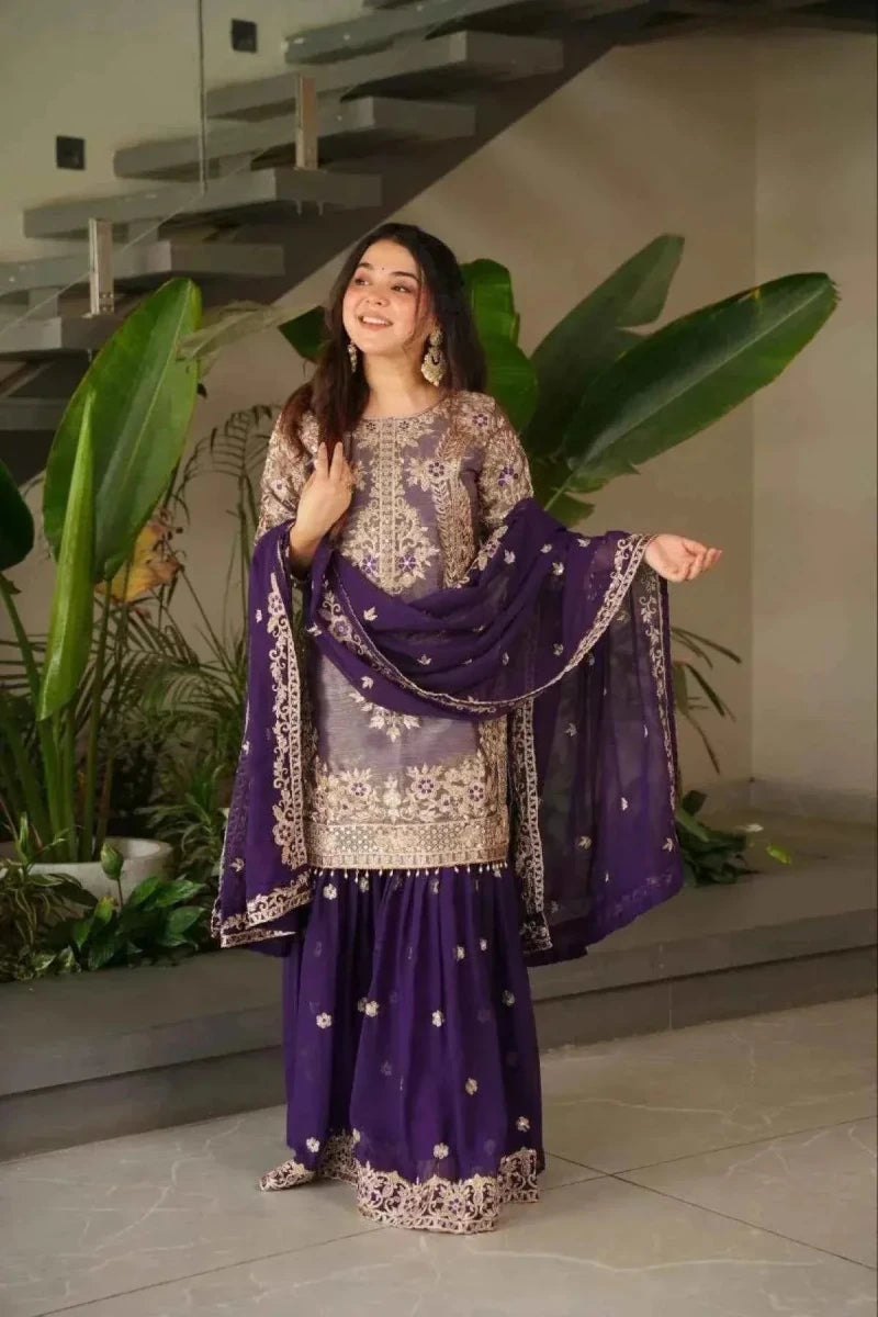 Purple embroidered sharara suit with long tunic and flared skirt, holding a dark dupatta