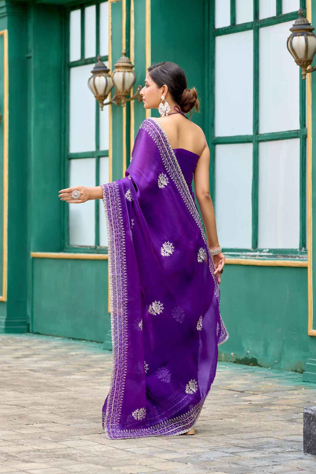Woman in elegant purple chiffon saree with silver embroidery standing outdoors by green wall