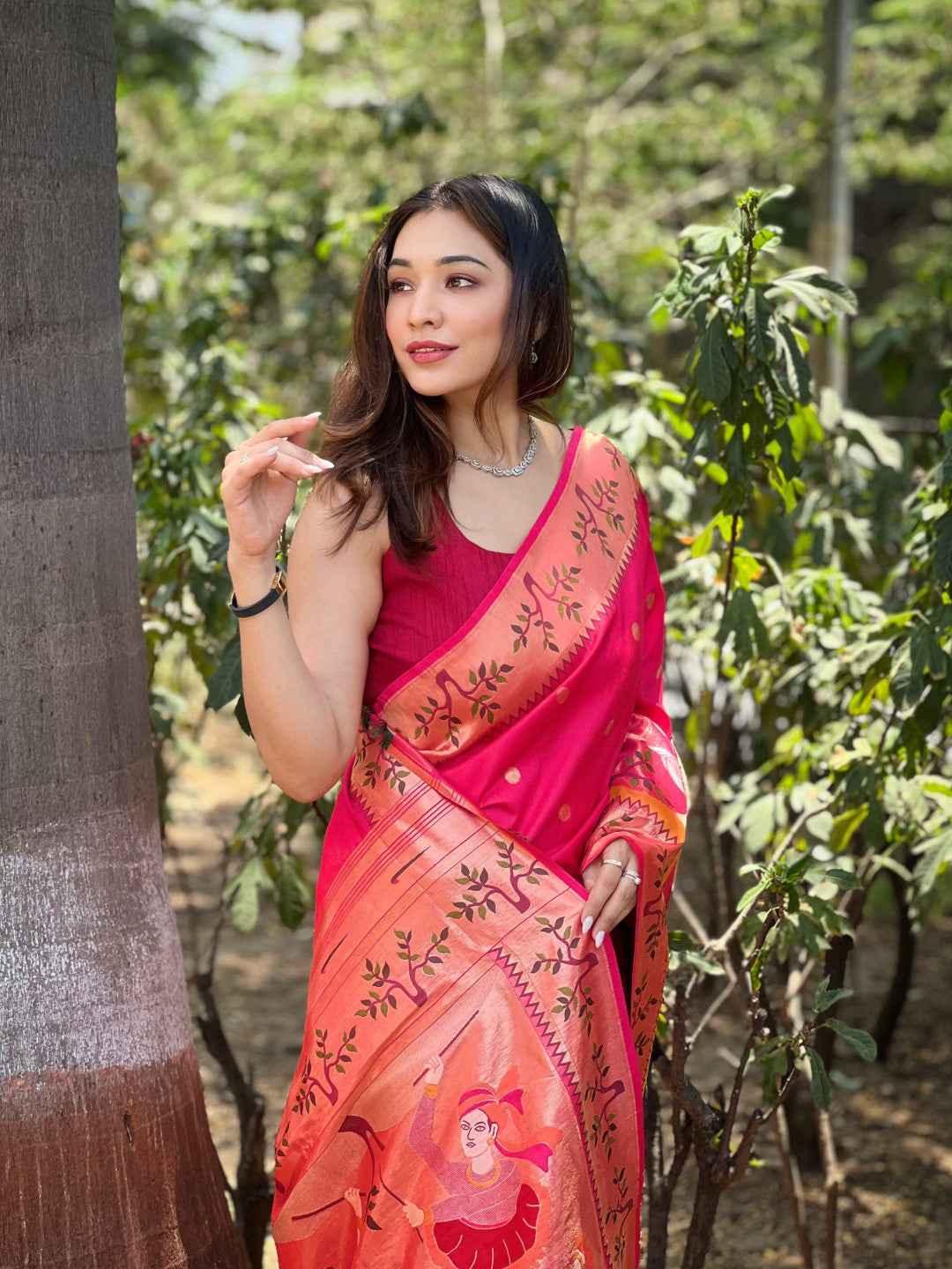 Woman wearing a vibrant rani pink Paithani silk saree with intricate zari weaving and traditional art design, posing outdoors