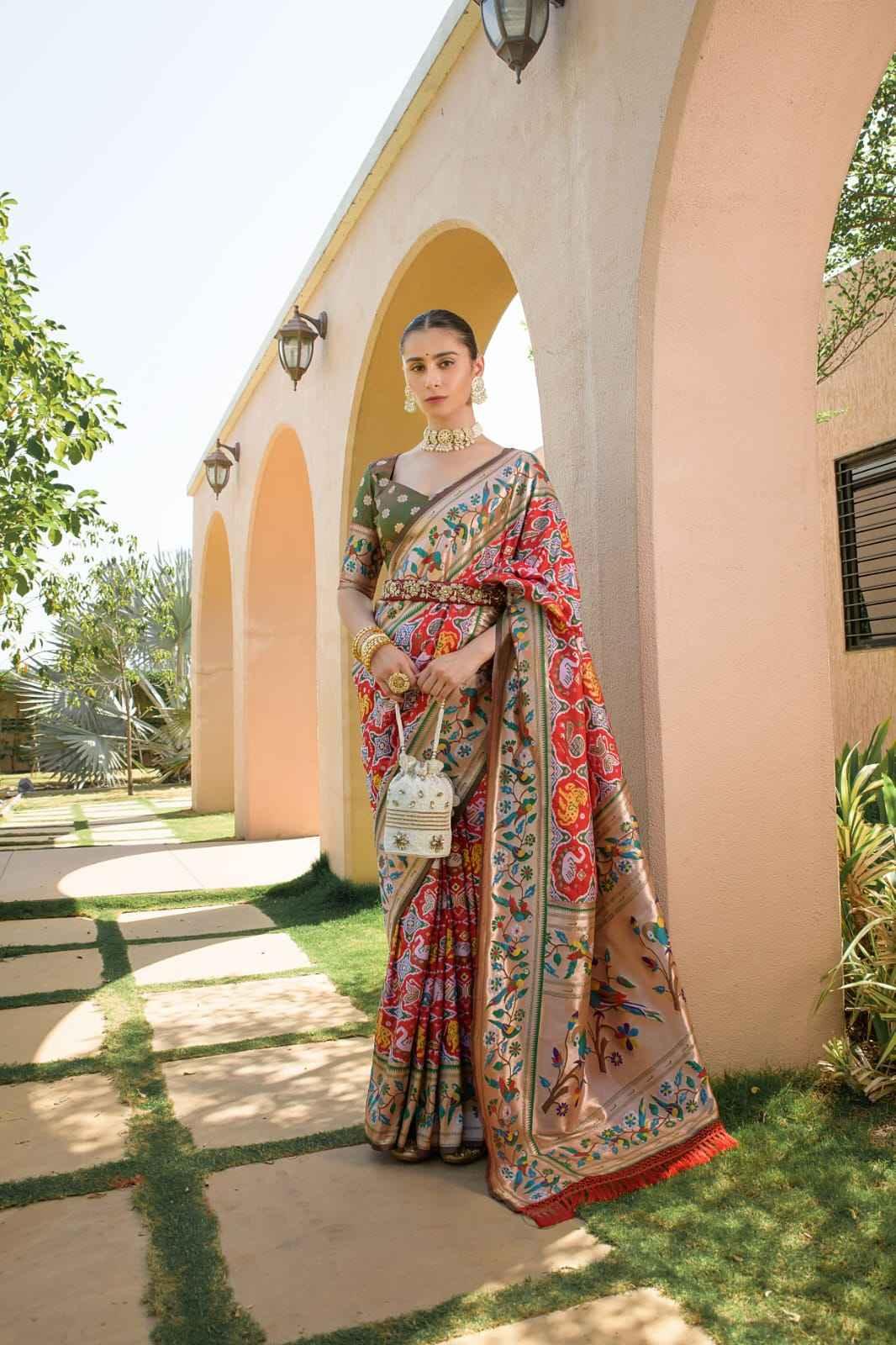 Woman wearing red and gold Paithani silk saree with floral zari patterns standing by arched walkway outdoors