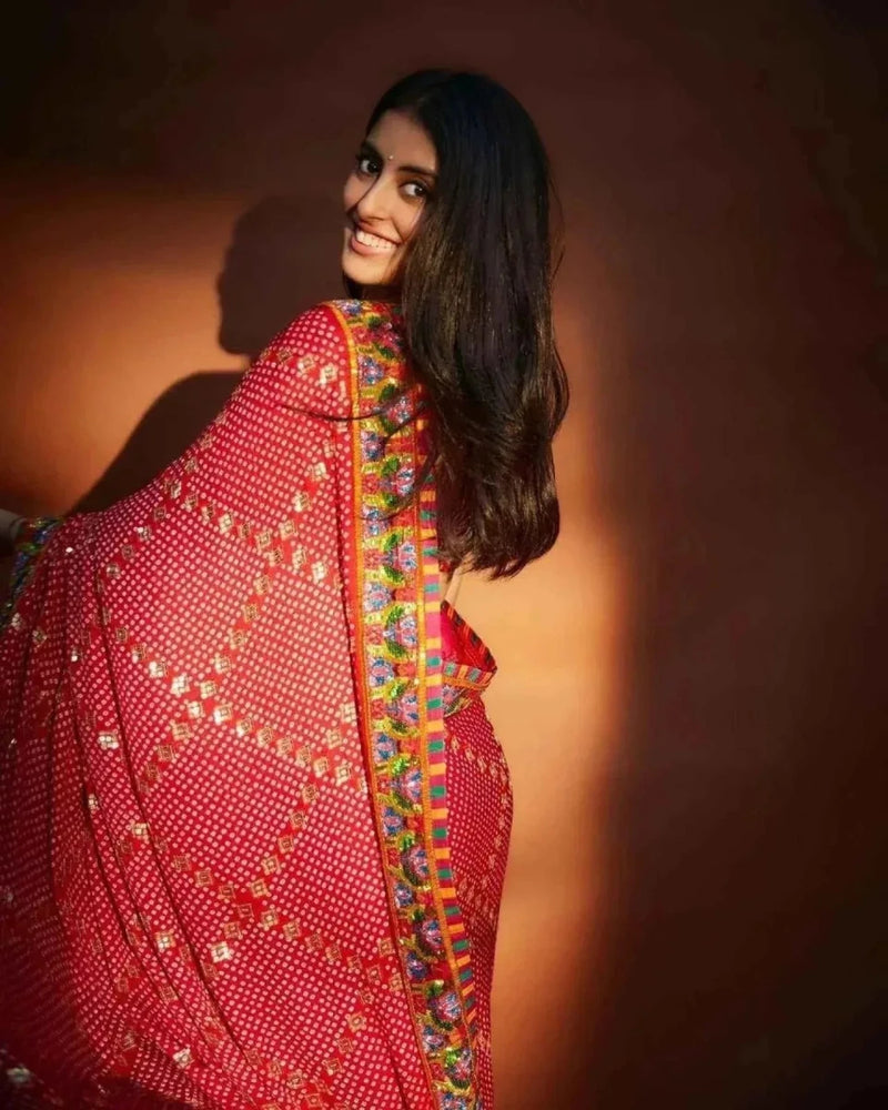 Red saree drape with bandhani motifs, bright multicolor border, and sequins