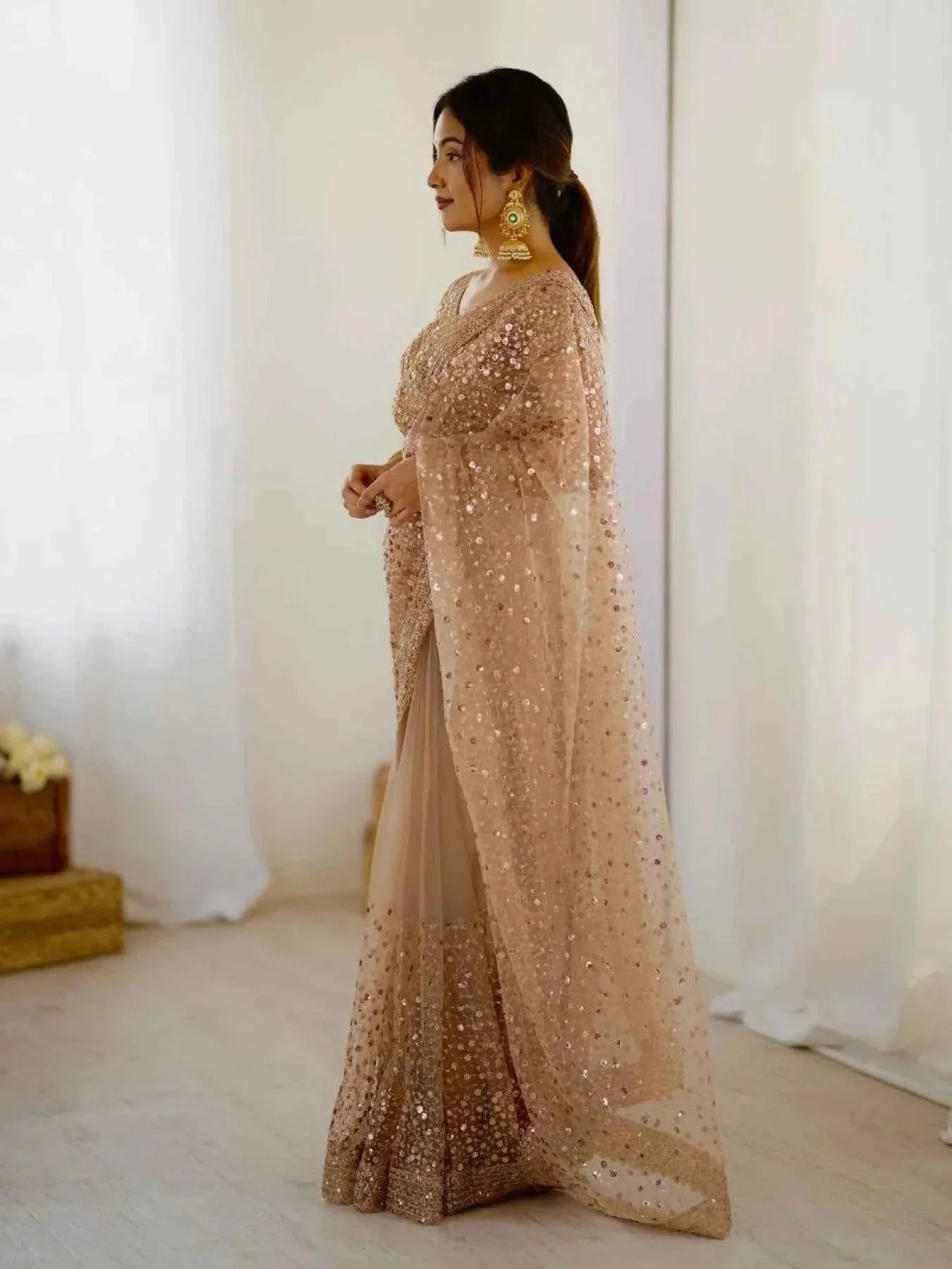 Woman wearing a rose gold net saree with all over sequin dori embroidery and gold earrings