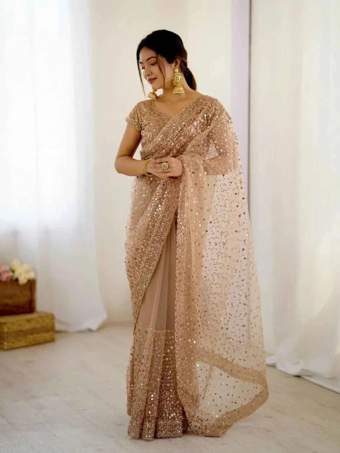 Woman wearing rose gold net saree with all over sequin and dori embroidery, posing indoors