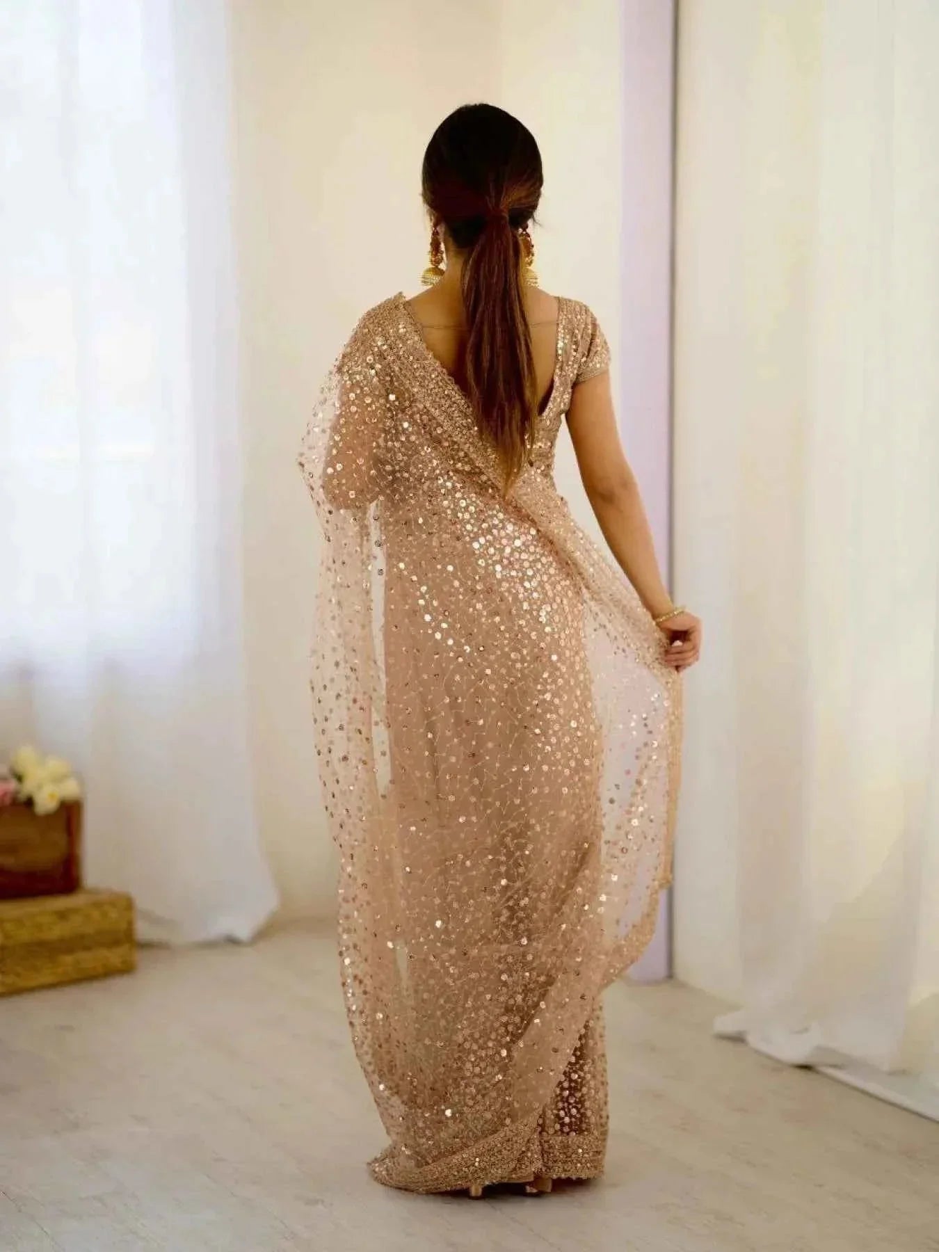Woman wearing rose gold net saree with sequin dori embroidery, standing indoors with light background