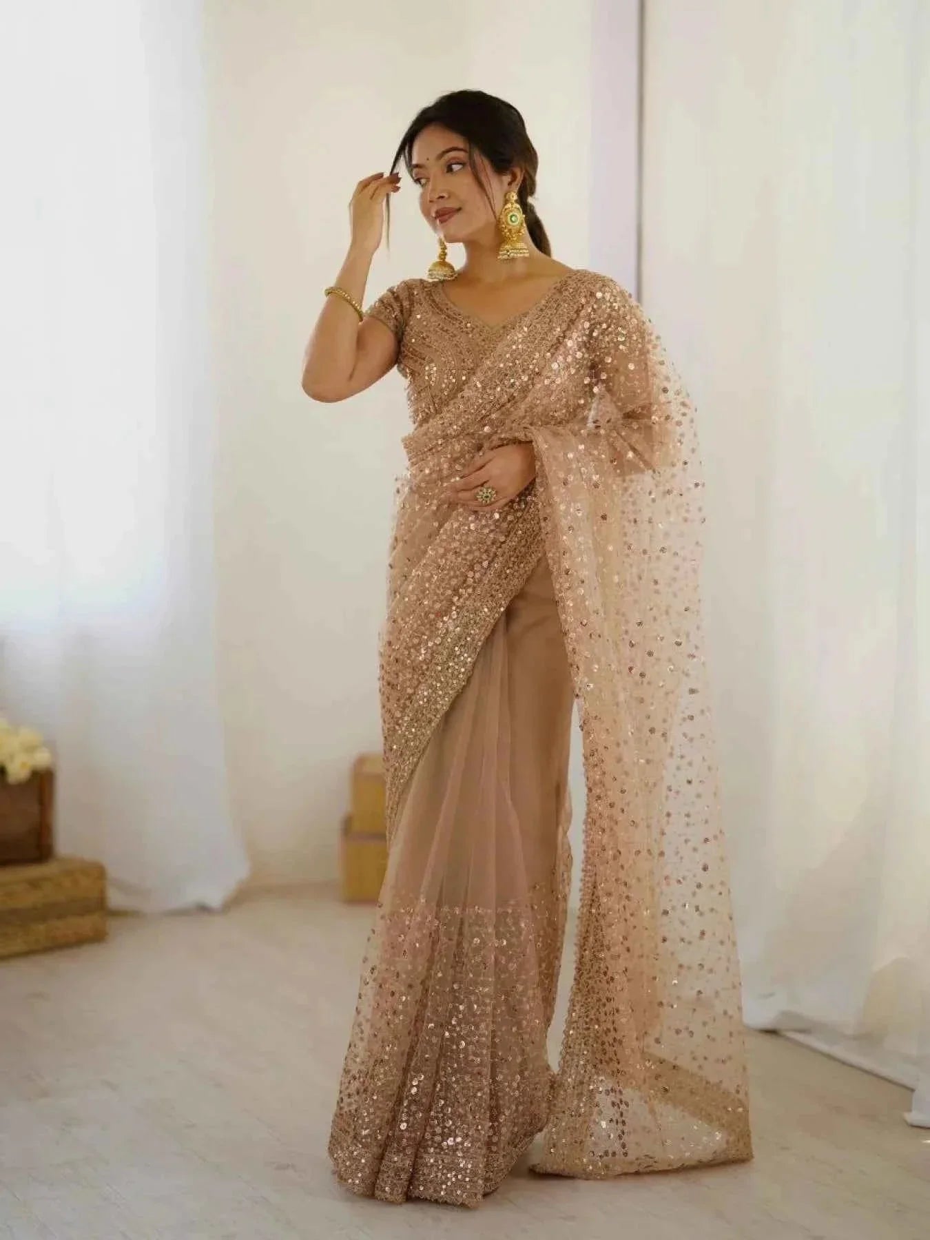 Woman wearing rose gold net saree with all-over sequin dori embroidery and gold jewelry