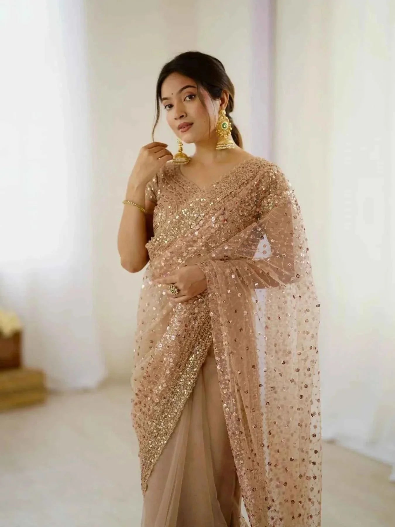 Woman wearing rose gold net saree with sequin dori embroidery and golden earrings