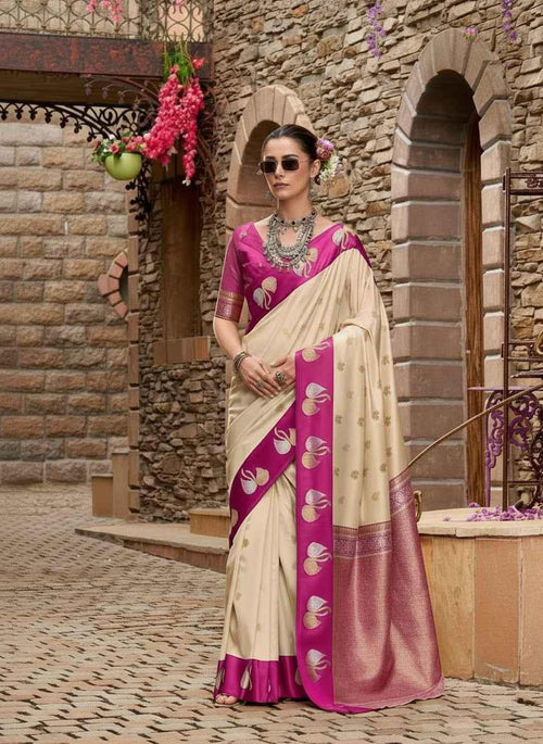 Woman wearing cream and pink silk saree with floral motifs, standing against stone wall with flowers