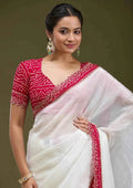 Woman wearing white tissue saree with red Bandhani blouse and gold earrings against green background