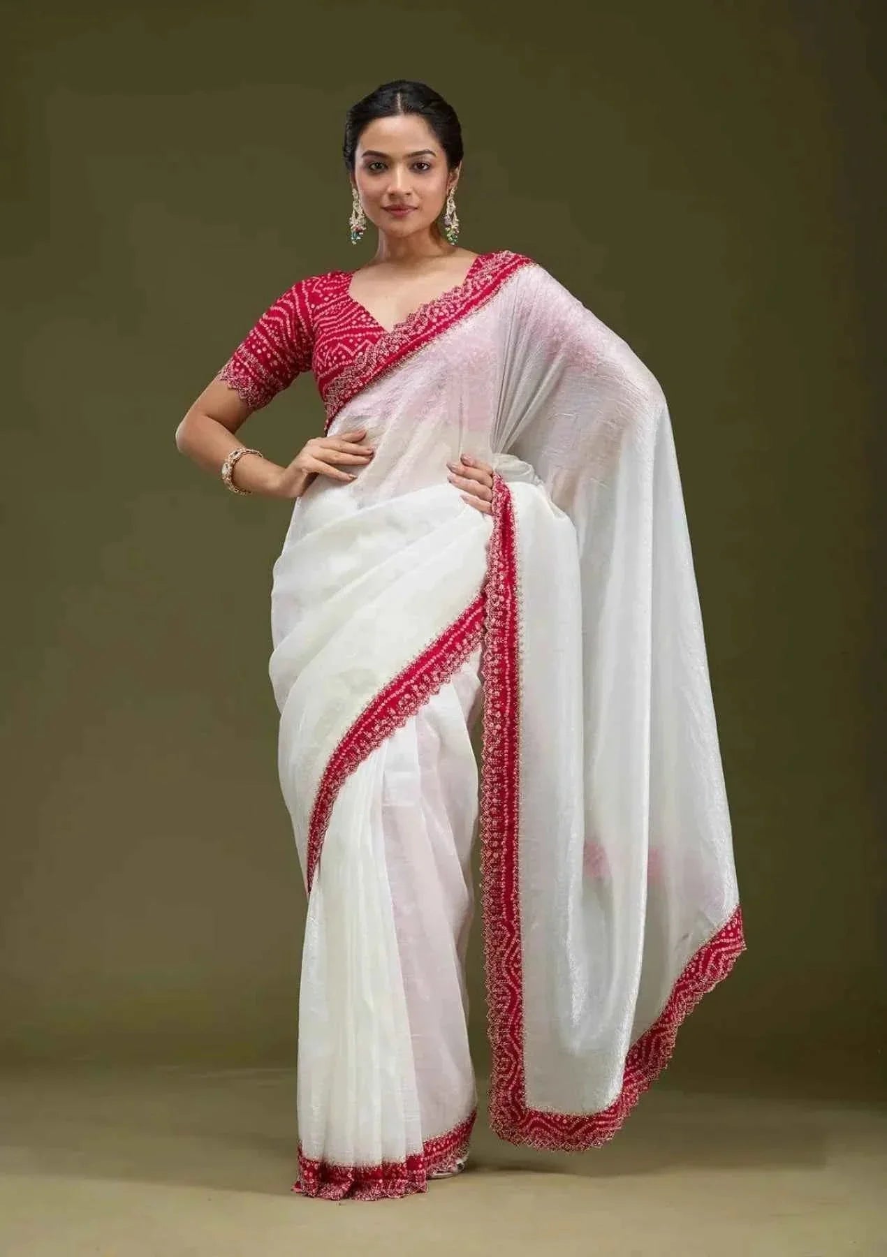 Woman wearing white tissue saree with red Bandhani blouse and red border, standing against plain background