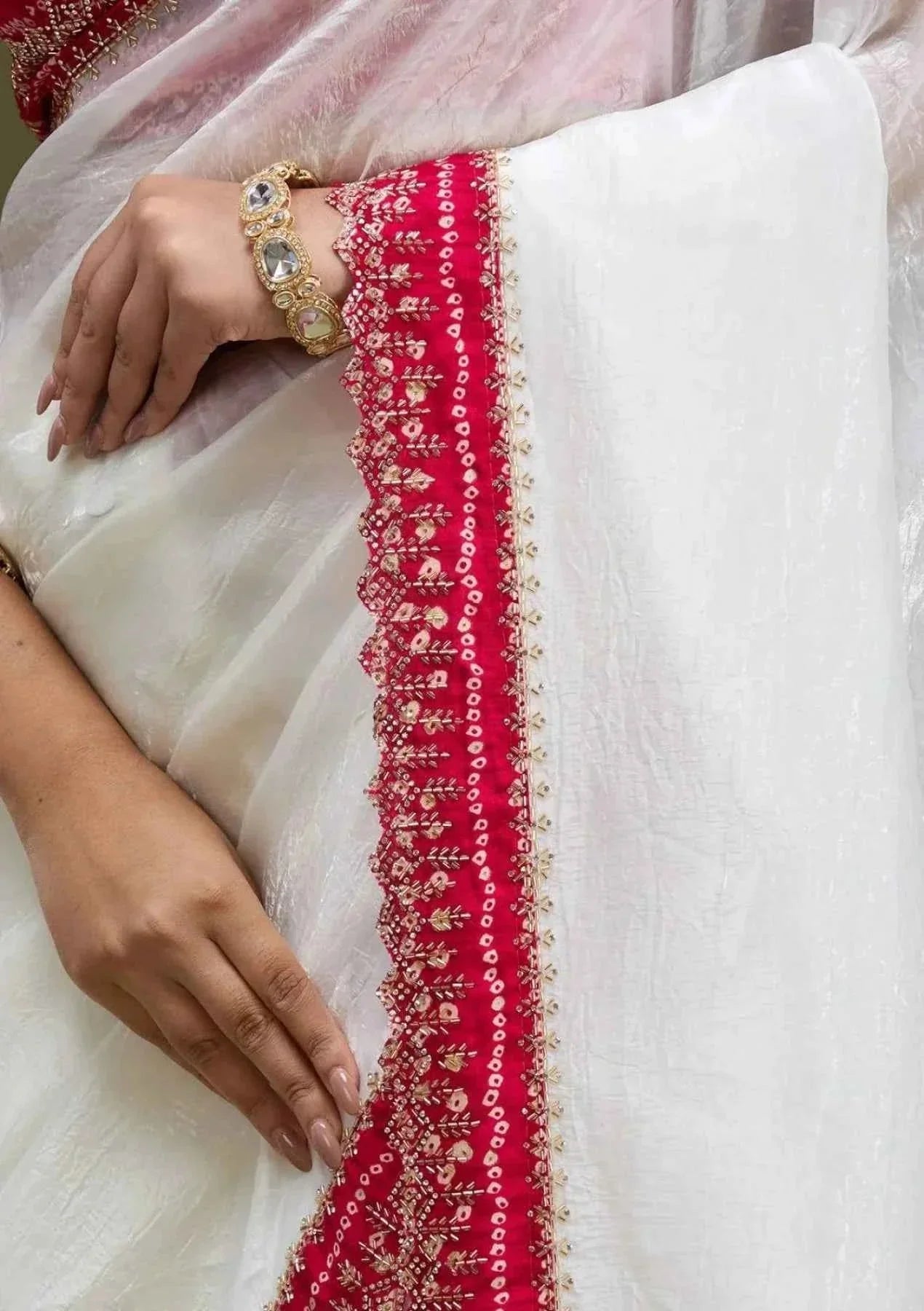White tissue saree with intricate red bandhani embroidered border and gold bracelet on hand