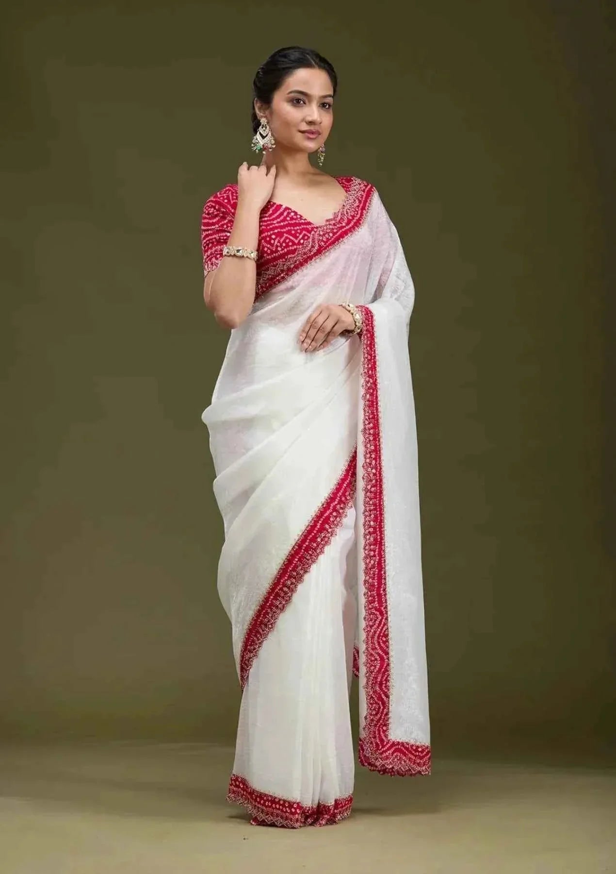 Woman wearing elegant white saree with red Bandhani border and matching red blouse on plain background