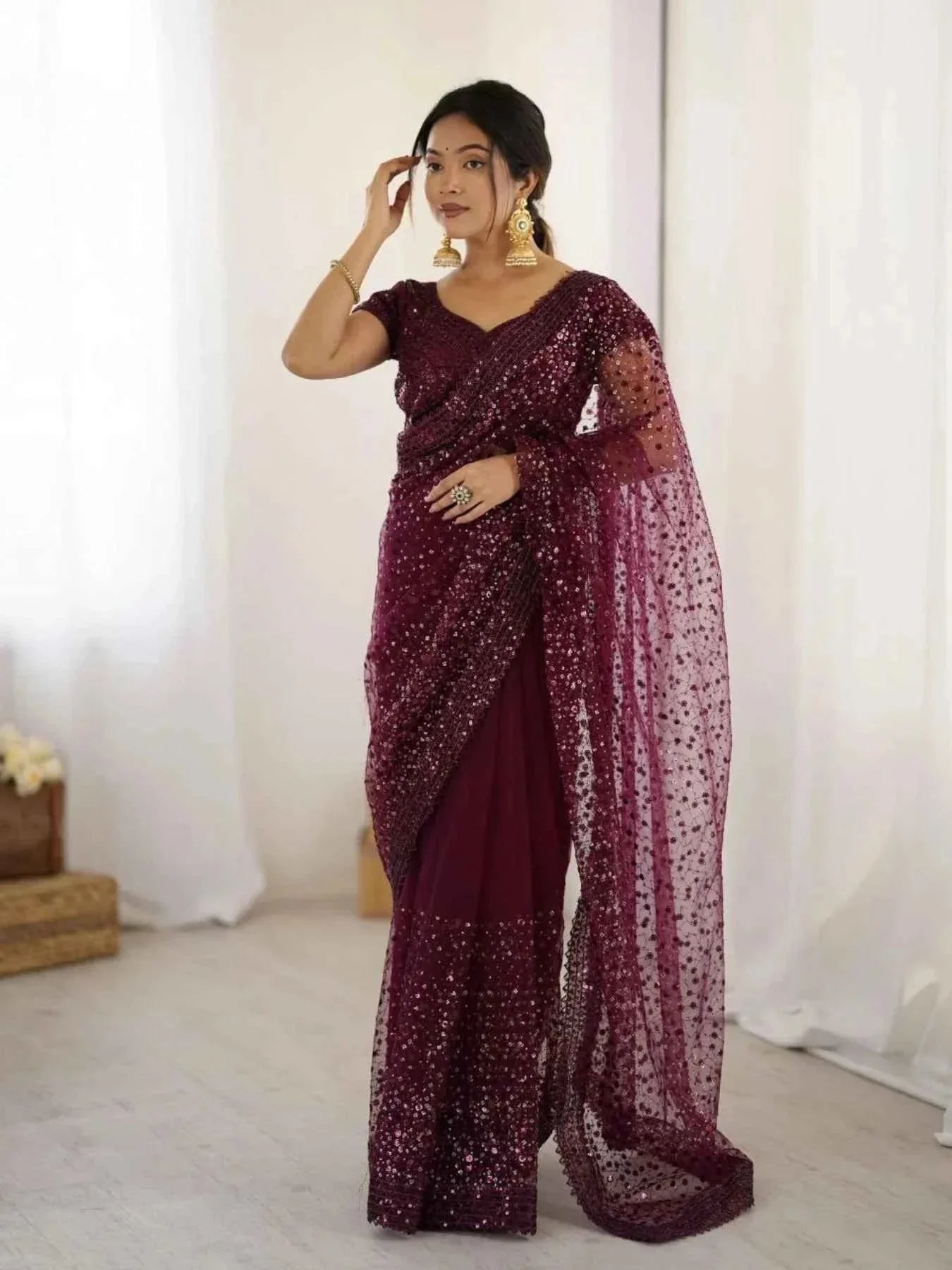 Woman wearing a wine net saree with all-over sequin dori embroidery and gold earrings