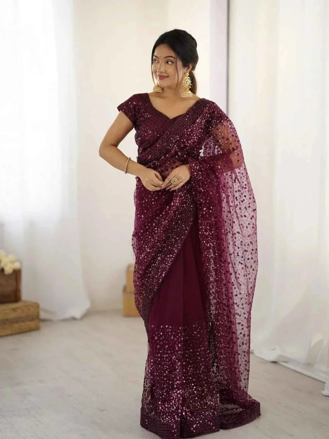 Woman wearing a wine net saree with all-over sequin Dori embroidery and gold jhumka earrings