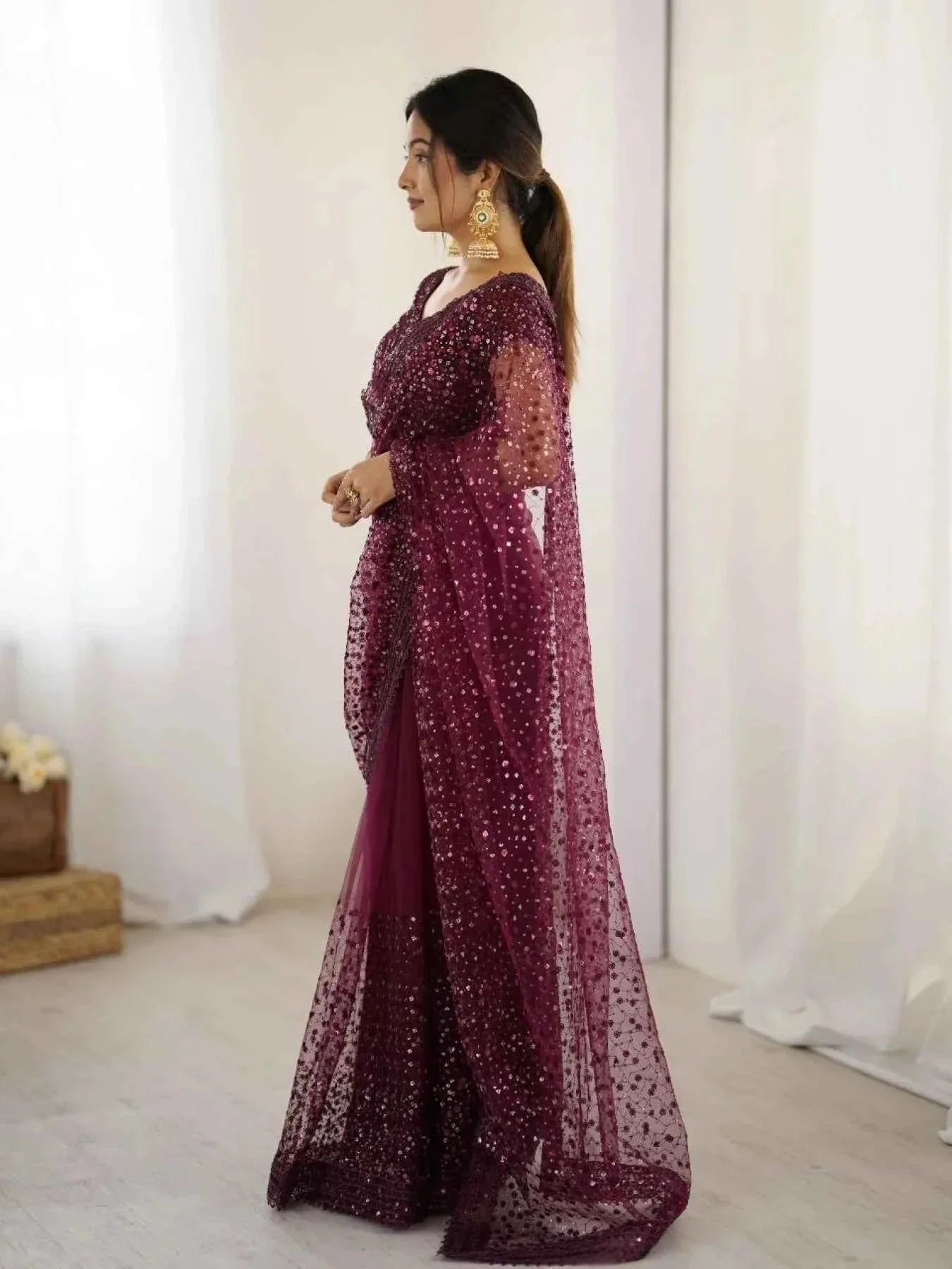 Woman in a wine net saree embellished with all-over sequins and dori embroidery, wearing gold jhumka earrings