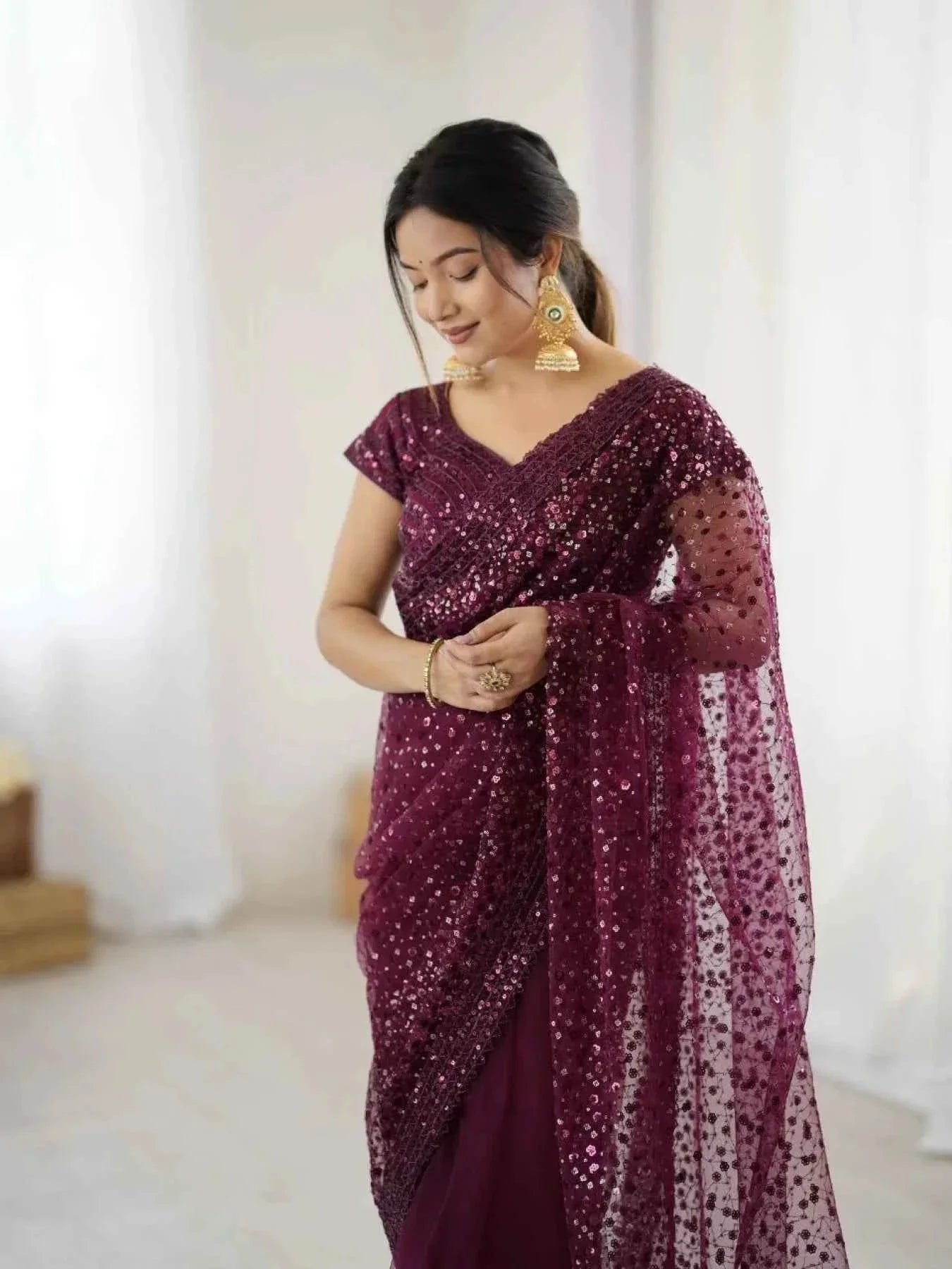 Woman wearing a wine net saree with all over sequin dori embroidery, paired with gold jhumka earrings