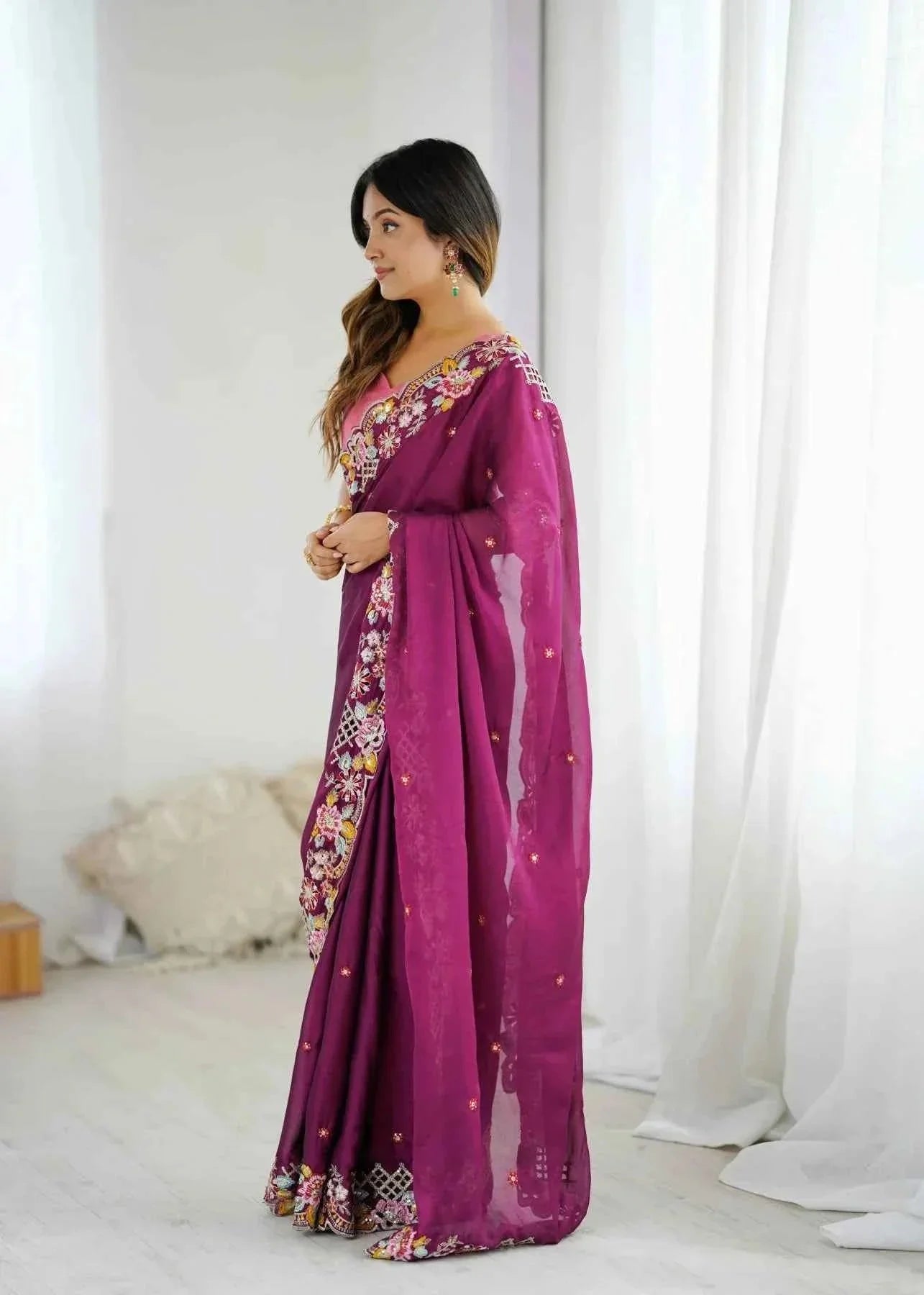 Woman in a wine-colored saree with sequin cutwork embroidery, posing indoors by white curtains