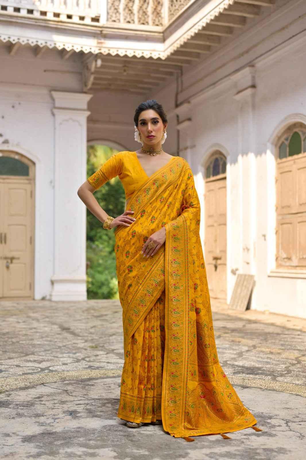 Woman in yellow pashmina silk saree with intricate Kashmiri jal embroidery standing in historic courtyard