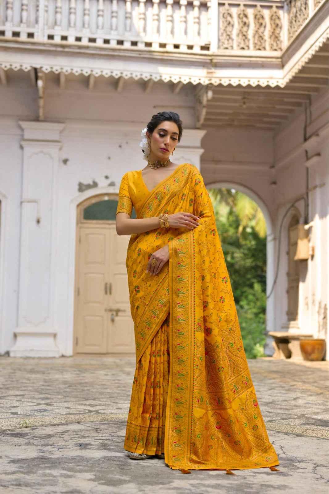 Woman wearing a yellow Kashmiri pashmina silk saree with intricate floral weaving in a traditional courtyard